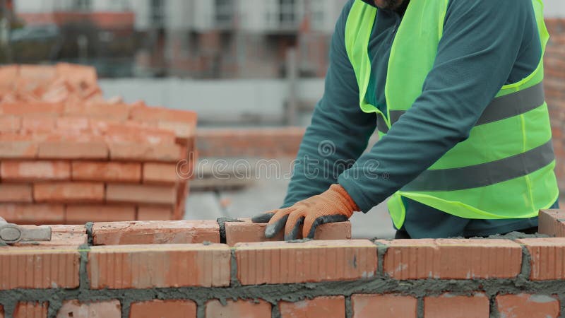 Un ouvrier du bâtiment pose des briques sur un mur Closeudo d'un ouvrier du bâtiment un mur de brique avec une passerelle sur un m banque de vidéos