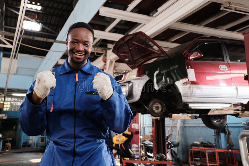 Un ouvrier mécanicien noir joyeux agissant avec un sourire dans le garage de la voiture fixe. images stock