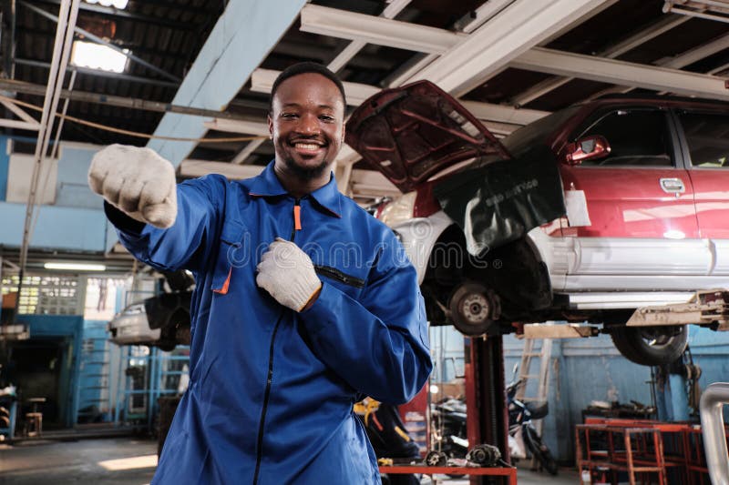 Un ouvrier mécanicien noir joyeux agissant avec un sourire dans le garage de la voiture fixe. images stock
