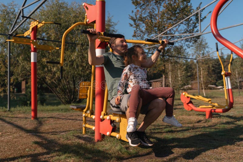 Un padre e una figlia condividono un momento gioioso facendo esercizio di palestra all'aperto circondata da verde e luce del sole fotografia stock libera da diritti
