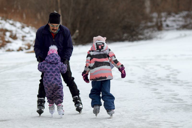 Un padre enseña a dos niñas a patinar en un lago helado en un día de invierno foto de archivo libre de regalías