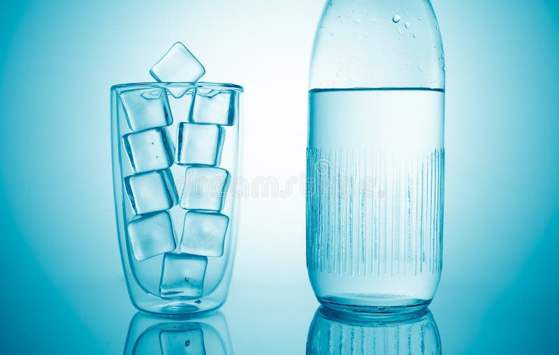 Un pahar cu cuburi de gheață și o sticlă cu apă potabilă proaspătă pe fond albastru stock photo