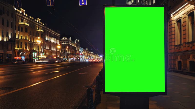 Un panneau d'affichage avec un écran vert sur une rue occupée de nuit banque de vidéos
