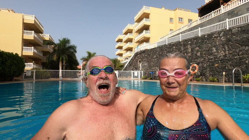 Un par de adultos mayores disfrutando del verano y divirtiéndose juntos en la piscina y sonriendo mirando a la cámara alegre feliz metrajes