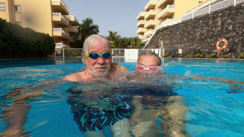 Un par de adultos mayores disfrutando del verano y divirtiéndose juntos en la piscina y sonriendo mirando a la cámara alegre feliz almacen de metraje de vídeo