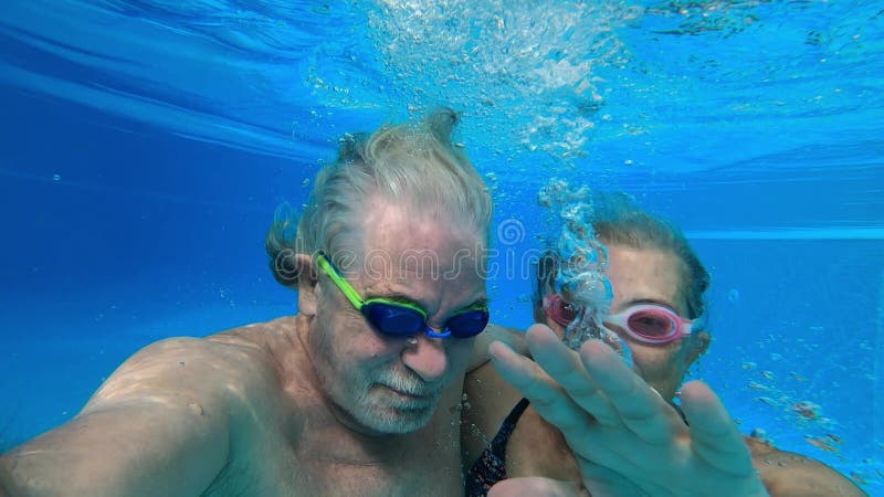 Un par de adultos mayores disfrutando del verano y divirtiéndose juntos en la piscina y sonriendo mirando a la cámara alegre feliz metrajes