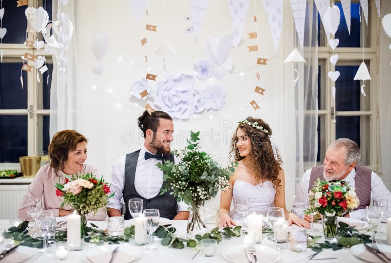 Un par joven con los padres que se sientan en una tabla en una boda, mirando uno a fotos de archivo Un par joven con los padres que se sientan en una tabla en una boda, mirando uno a fotos de archivo