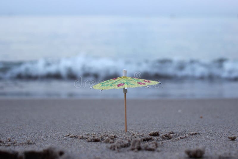 Un parapluie d'un cocktail dans le sable sur la plage dans la perspective des vagues de mer photo stock Un parapluie d'un cocktail dans le sable sur la plage dans la perspective des vagues de mer photo stock