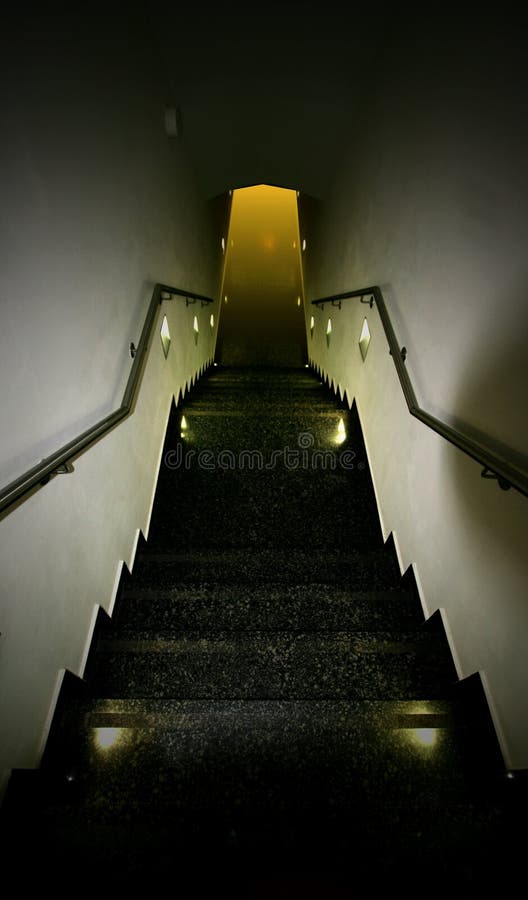 A walkway down a steep stairwell towards a source of light at the end. Concept of temptation and risk. A walkway down a steep stairwell towards a source of light at the end. Concept of temptation and risk.