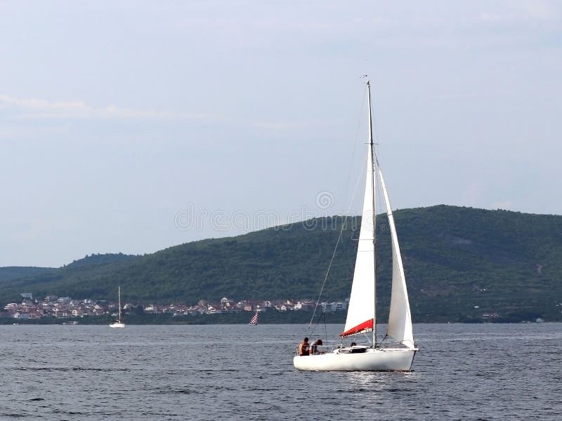 Un pequeño yate de los deportes de la navegación de la navegación diurna está navegando con tres dueños de un yate a lo largo de imagen de archivo libre de regalías Un pequeño yate de los deportes de la navegación de la navegación diurna está navegando con tres dueños de un yate a lo largo de imagen de archivo libre de regalías