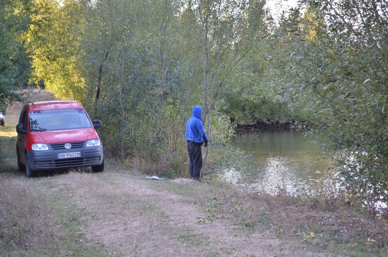 Un pescatore è in piedi vicino all'acqua e tiene in mano una canna volante con la mano destra L'uomo guarda dritto in avanti fotografia stock libera da diritti Un pescatore è in piedi vicino all'acqua e tiene in mano una canna volante con la mano destra L'uomo guarda dritto in avanti fotografia stock libera da diritti