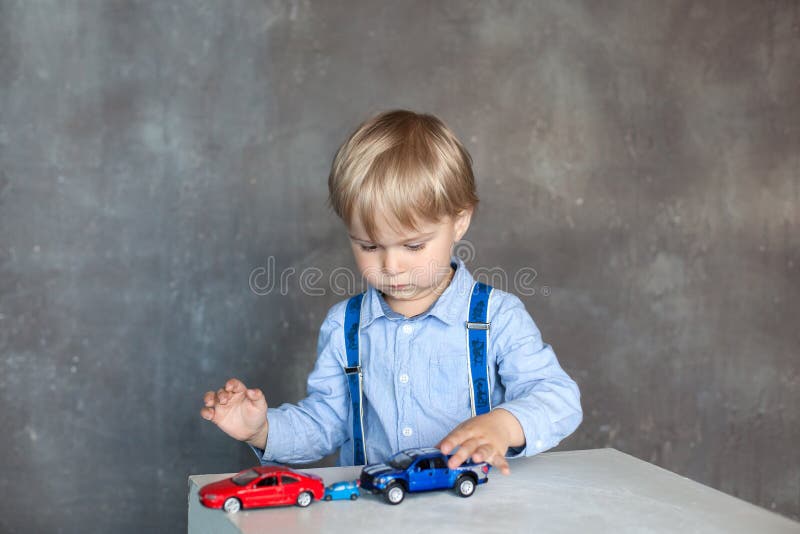 Un petit garçon dans une chemise avec des bretelles joue avec les voitures colorées multi de jouet de jouet Garçon préscolaire jo photos stock Un petit garçon dans une chemise avec des bretelles joue avec les voitures colorées multi de jouet de jouet Garçon préscolaire jo photos stock