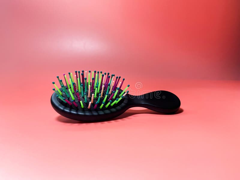 Un piccolo pennello con setole colorate giace su una superficie rosa. Pennello compatto con maniglia di legno nera e setole multicolori vibranti è posizionato su uno sfondo rosa morbido. il pennello ha una forma ovale e una maniglia leggermente curva per una comoda presa.