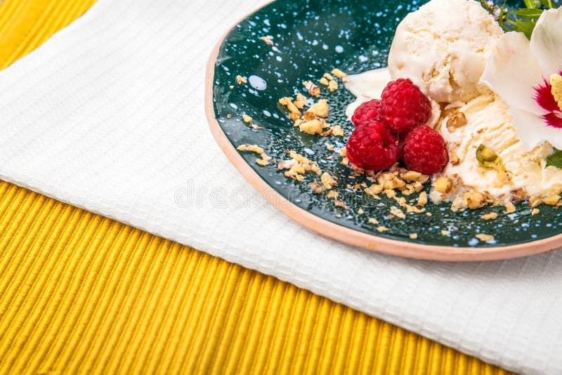 Un plat complètement d'une crème glacée avec les framboises roses douces sur un tissu blanc et sur une nappe jaune Casse-croûte d photos stock Un plat complètement d'une crème glacée avec les framboises roses douces sur un tissu blanc et sur une nappe jaune Casse-croûte d photos stock