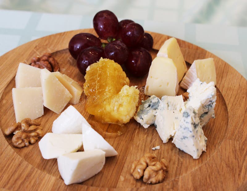 Un plat en bois avec des raisins de parmesan avec les noix et le miel images libres de droits Un plat en bois avec des raisins de parmesan avec les noix et le miel images libres de droits