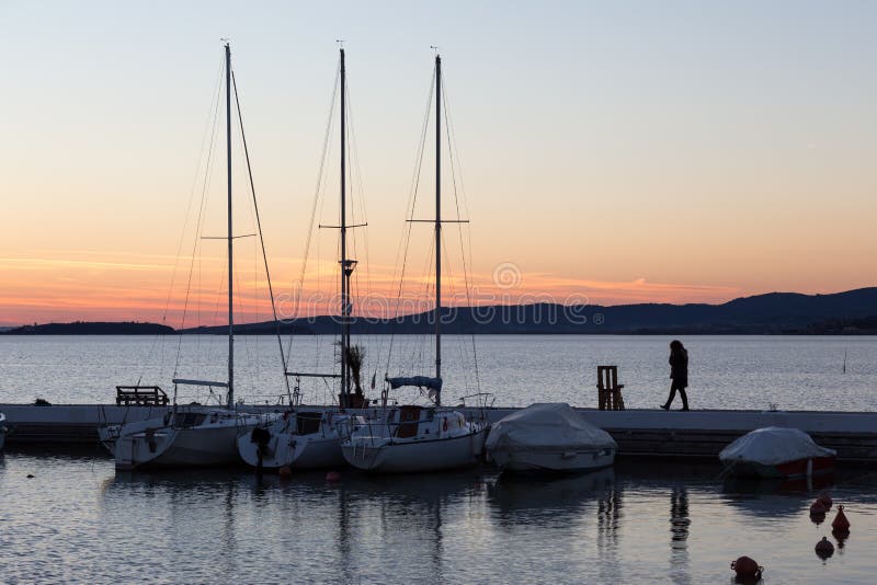 Un port sur un lac au coucher du soleil, avec les divers bateaux et une femme t image stock Un port sur un lac au coucher du soleil, avec les divers bateaux et une femme t image stock