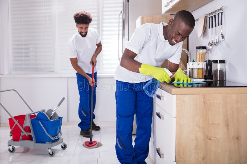 Un portiere maschio sorridente Cleaning The Kitchen di due giovani immagine stock Un portiere maschio sorridente Cleaning The Kitchen di due giovani immagine stock