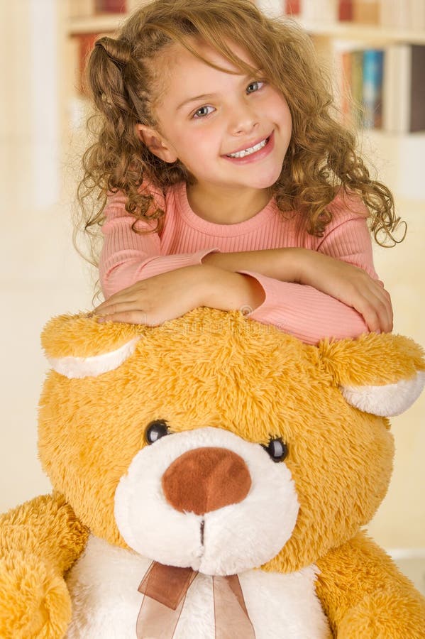 Un portrait d'une jeune jolie fille souriant et posant au-dessus de sa tête de l'ours de nounours s à un arrière-plan de bureau d images libres de droits Un portrait d'une jeune jolie fille souriant et posant au-dessus de sa tête de l'ours de nounours s à un arrière-plan de bureau d images libres de droits