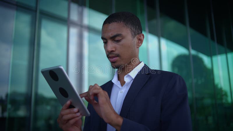 Un profesional de negocios que utiliza con confianza una tableta mientras se encuentra fuera de un edificio moderno almacen de video