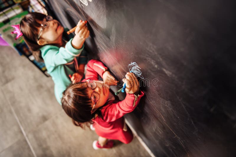 Un punto di vista superiore di due bambini soleggiati che indossano i vetri che attingono lavagna fotografia stock libera da diritti Un punto di vista superiore di due bambini soleggiati che indossano i vetri che attingono lavagna fotografia stock libera da diritti