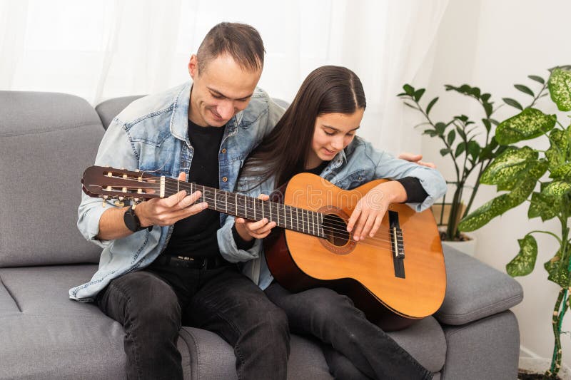 Un père qui enseigne à une fille adolescente la guitare à la maison. Cours de musique familiale avec instrument à cordes photos stock