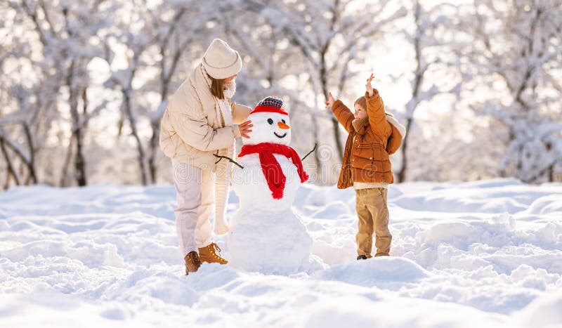 Un ragazzino carino che fa un pupazzo di neve con la mamma nel parco invernale