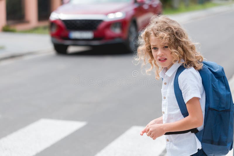 Un ragazzino con uno zainetto blu attraversa la strada immagine stock