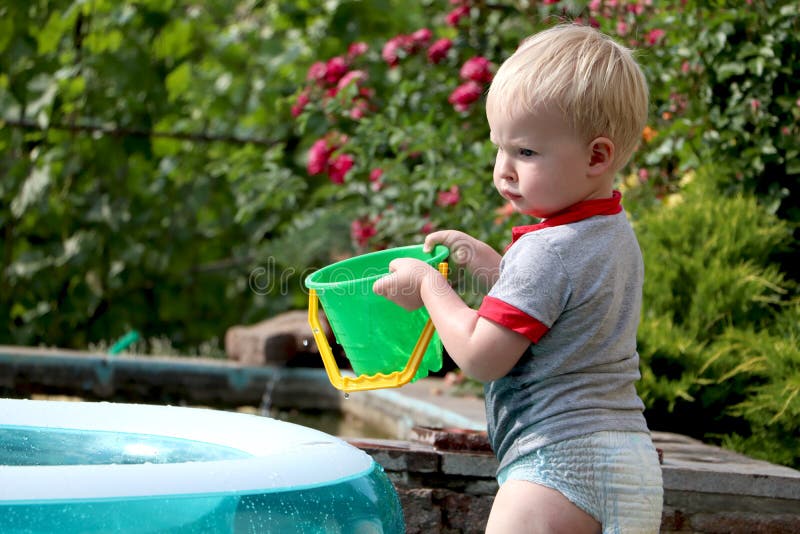 Un ragazzino sta giocando con acqua vicino ad uno stagno gonfiabile Feste della famiglia e di estate Infanzia felice fotografia stock libera da diritti Un ragazzino sta giocando con acqua vicino ad uno stagno gonfiabile Feste della famiglia e di estate Infanzia felice fotografia stock libera da diritti