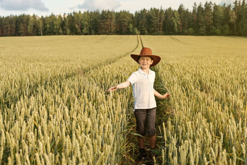 Un ragazzo cammina al giacimento di grano in un cappello da cowboy immagine stock libera da diritti Un ragazzo cammina al giacimento di grano in un cappello da cowboy immagine stock libera da diritti
