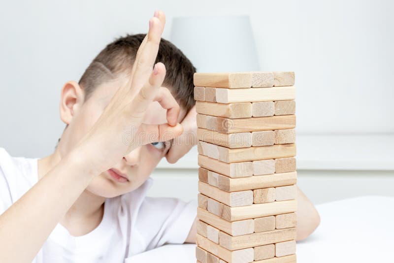 Un ragazzo caucasico preteen annoiato che prova a giocare il gioco da tavolo di legno della torre del blocco per intrattenersi fotografie stock Un ragazzo caucasico preteen annoiato che prova a giocare il gioco da tavolo di legno della torre del blocco per intrattenersi fotografie stock