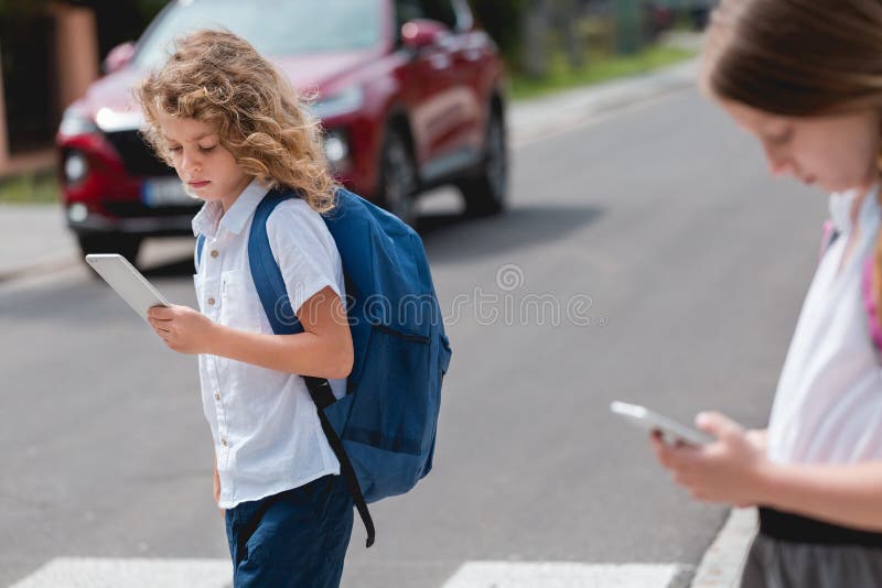 Un ragazzo con uno zaino e un cellulare passa attraverso la traversata pedonale senza guardare le auto rosse lo fanno passare immagine stock
