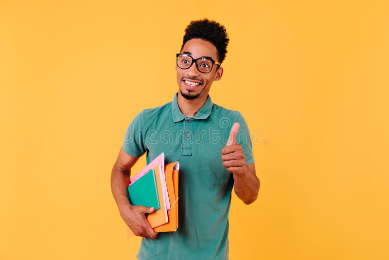 Un ragazzo dai capelli dorati eccitato che tiene in mano libri. studio di uno studente africano disinteressato immagine stock libera da diritti