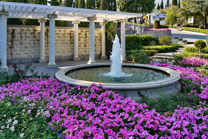 Un regard chic d'un beau parterre avec l'horticulture rose autour d'une fontaine de battre dans une cuvette concrète sur a photographie stock Un regard chic d'un beau parterre avec l'horticulture rose autour d'une fontaine de battre dans une cuvette concrète sur a photographie stock