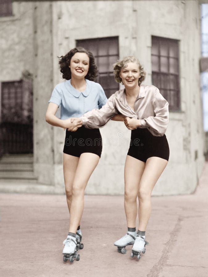 Un ritratto di due giovani donne con le lame del rullo che pattinano sulla strada e sorridere (tutte le persone rappresentate non