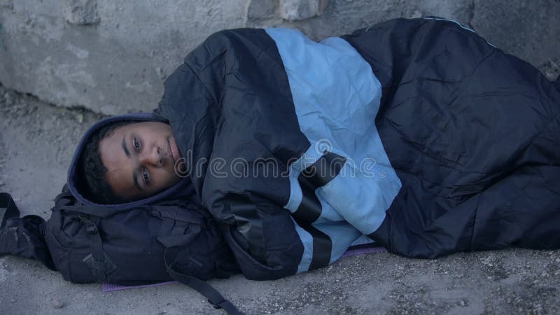 Un rÃ©fugiÃ© africain allongÃ© dans la rue recouvert d'un sac de couchage, sans abri