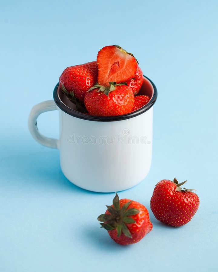 Un sacco di fragole fresche mature rosse in una tazza bianca smaltata su sfondo blu immagini stock libere da diritti Un sacco di fragole fresche mature rosse in una tazza bianca smaltata su sfondo blu immagini stock libere da diritti