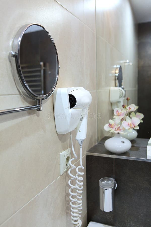 Un secador de pelo cuelga en la pared Foto en el interior Flores y un espejo están fuera de foco El concepto de negocio hotelero fotografía de archivo libre de regalías Un secador de pelo cuelga en la pared Foto en el interior Flores y un espejo están fuera de foco El concepto de negocio hotelero fotografía de archivo libre de regalías