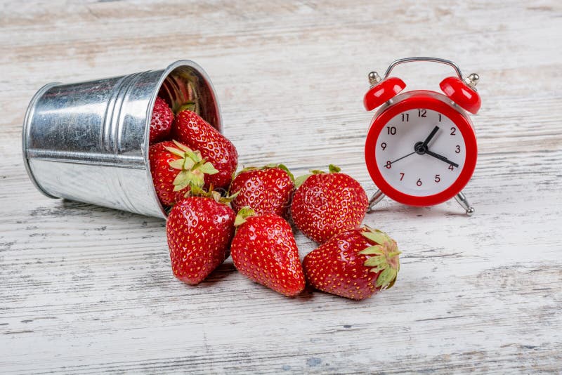 Un secchio delle fragole mature fresche e un secchio rosso della sveglia A delle fragole mature fresche e di una sveglia rossa fotografia stock libera da diritti Un secchio delle fragole mature fresche e un secchio rosso della sveglia A delle fragole mature fresche e di una sveglia rossa fotografia stock libera da diritti