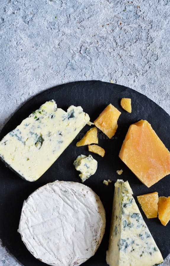 Un juego de quesos: queso azul, parmesano, camembert sobre pizarra. Platos con manjares. Ver desde arriba imagenes de archivo Un juego de quesos: queso azul, parmesano, camembert sobre pizarra. Platos con manjares. Ver desde arriba imagenes de archivo