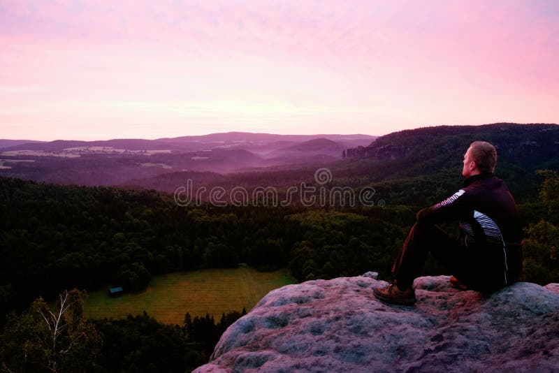 Un sportif s'asseyent sur une roche et observer au paysage de matin ci-dessous photo libre de droits Un sportif s'asseyent sur une roche et observer au paysage de matin ci-dessous photo libre de droits