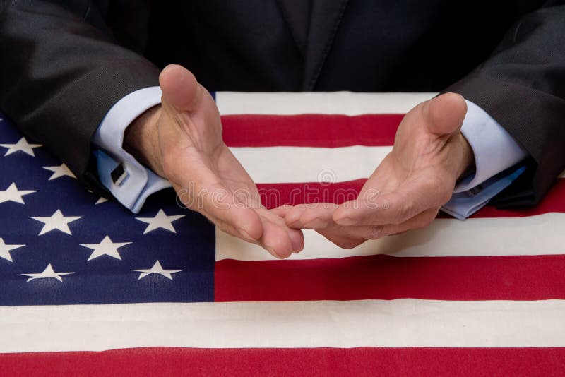 A un tavolo coperto da una bandiera americana, un uomo d'affari e un politico tiene le mani al dialogo immagini stock A un tavolo coperto da una bandiera americana, un uomo d'affari e un politico tiene le mani al dialogo immagini stock