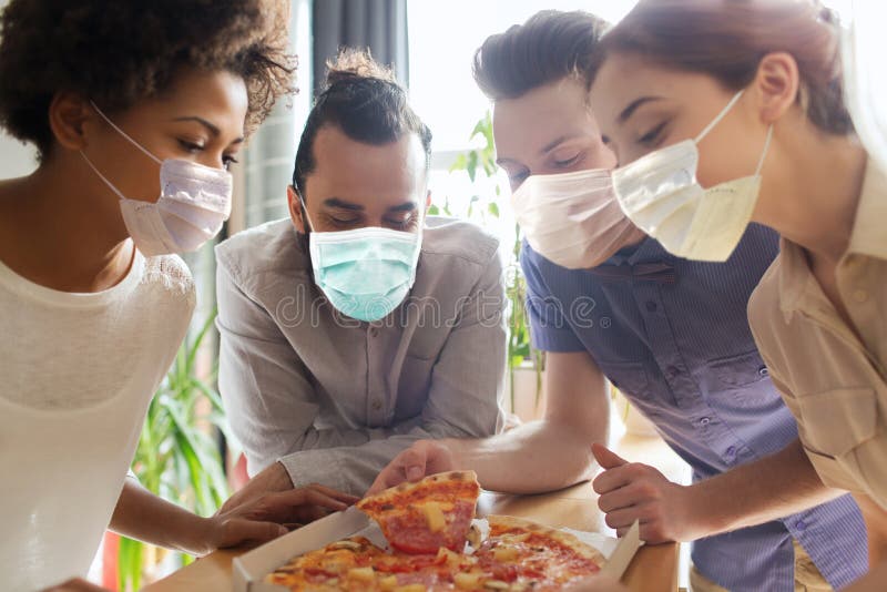 Un team di imprenditori mangia pizza in maschere per l'ufficio fotografie stock