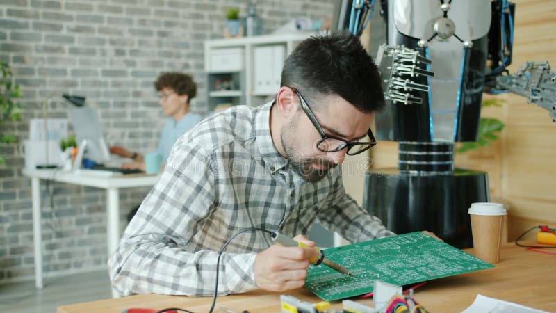 Un technicien masculin réparant une carte de microcircuit avec un robot de fabrication de soudure