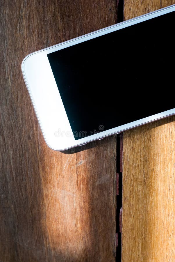 Un teléfono inteligente con pantalla apagada colocada sobre una mesa de madera marrón