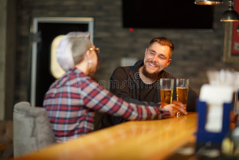Un tipo felice, sedentesi e parlante in una barra con una ragazza, una birra bevente e una risata all'interno fotografia stock Un tipo felice, sedentesi e parlante in una barra con una ragazza, una birra bevente e una risata all'interno fotografia stock