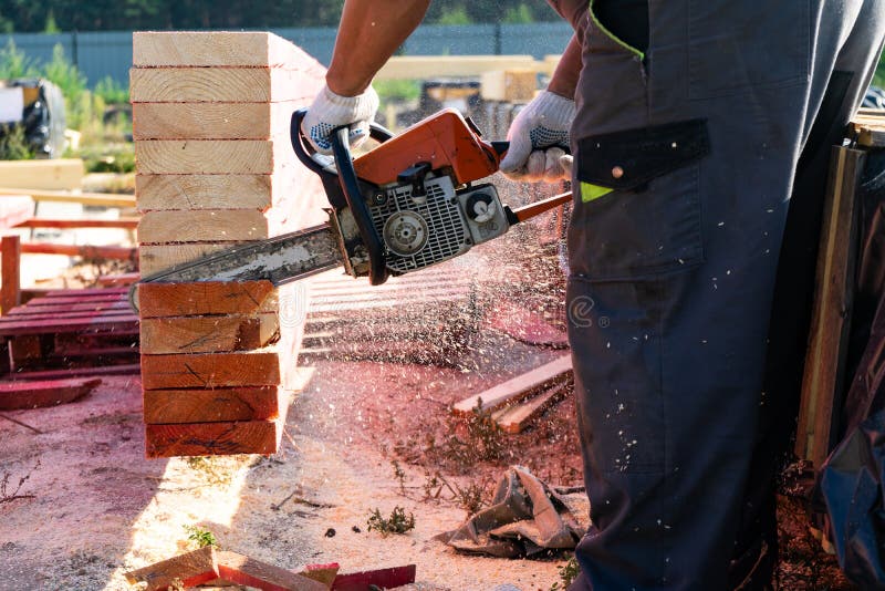 Un trabajador asierra de un tablero de madera de la motosierra Construcción de la casa foto de archivo Un trabajador asierra de un tablero de madera de la motosierra Construcción de la casa foto de archivo