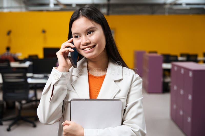 Un trabajador empresarial sonriente hablando por teléfono móvil en la oficina de openplan imagenes de archivo