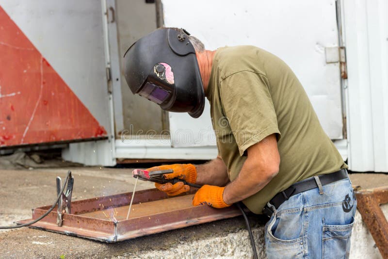 Un trabajador en una máscara de soldadura realiza el trabajo de soldadura sobre el metal Partes en enlace de metal bajo temperatu imagenes de archivo Un trabajador en una máscara de soldadura realiza el trabajo de soldadura sobre el metal Partes en enlace de metal bajo temperatu imagenes de archivo