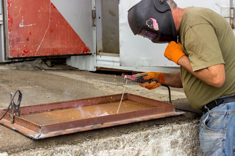 Un trabajador en una máscara de soldadura realiza el trabajo de soldadura sobre el metal Partes en enlace de metal bajo temperatu fotografía de archivo Un trabajador en una máscara de soldadura realiza el trabajo de soldadura sobre el metal Partes en enlace de metal bajo temperatu fotografía de archivo