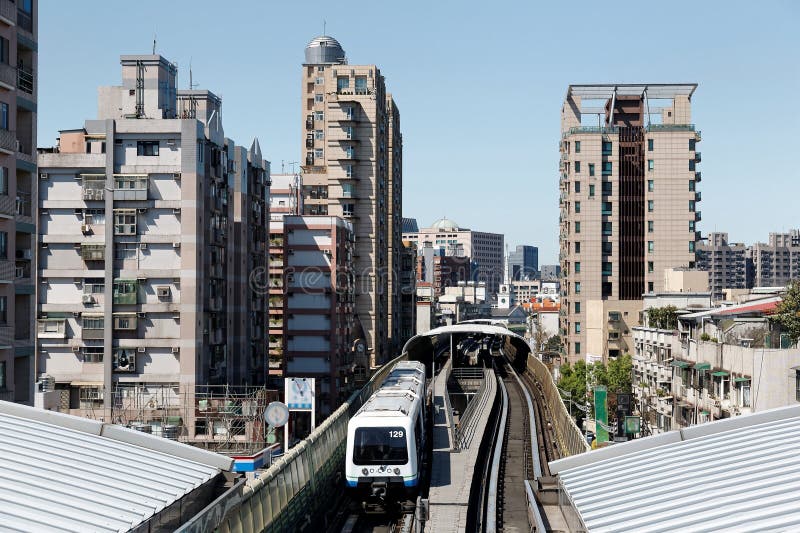 Un train de métro voyage sur les rails élevés entre les tours de bureau et les blocs résidentiels, arrivant à une station de syst photos libres de droits Un train de métro voyage sur les rails élevés entre les tours de bureau et les blocs résidentiels, arrivant à une station de syst photos libres de droits